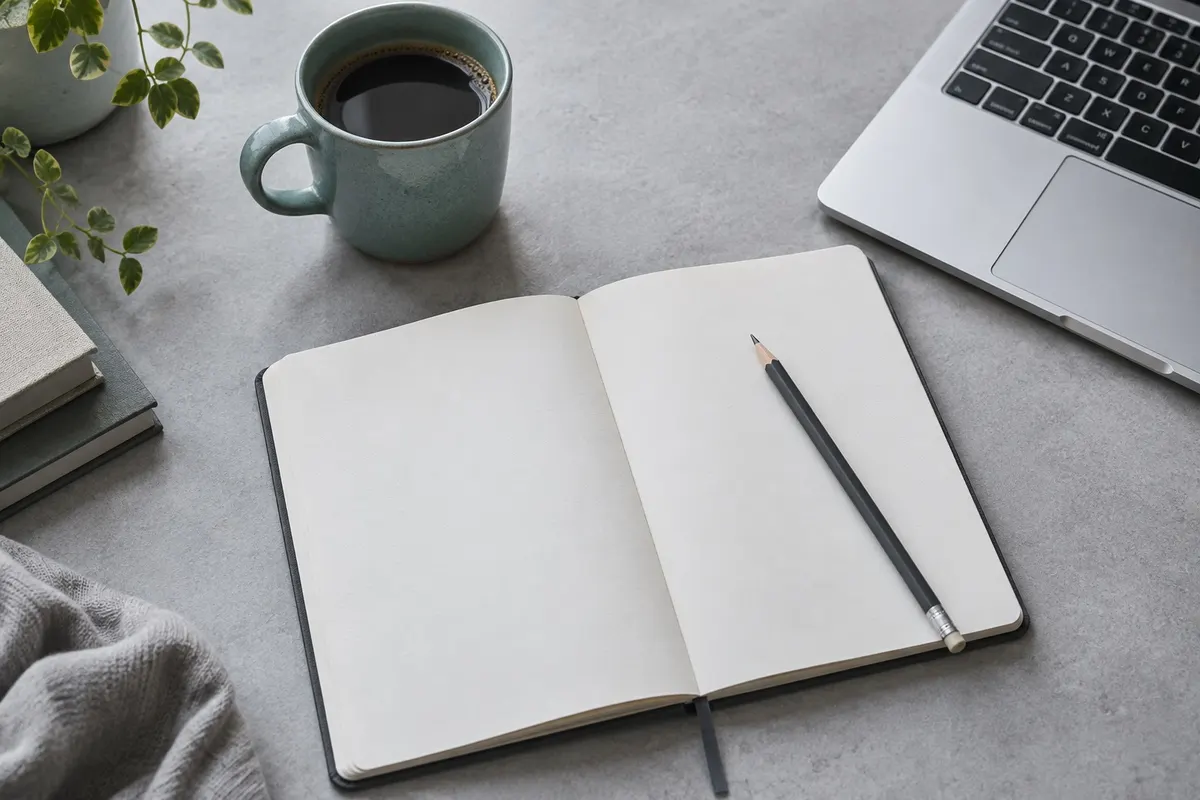 A quiet desk with a notebook, pencil and teal cup beside a laptop